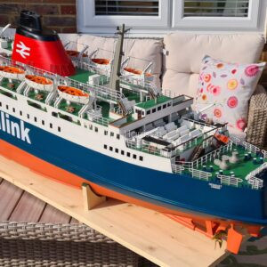 Large replica of a white, blue, and orange ferry, with details including lifeboats, seating, pullies, and flag. It's on a patio table