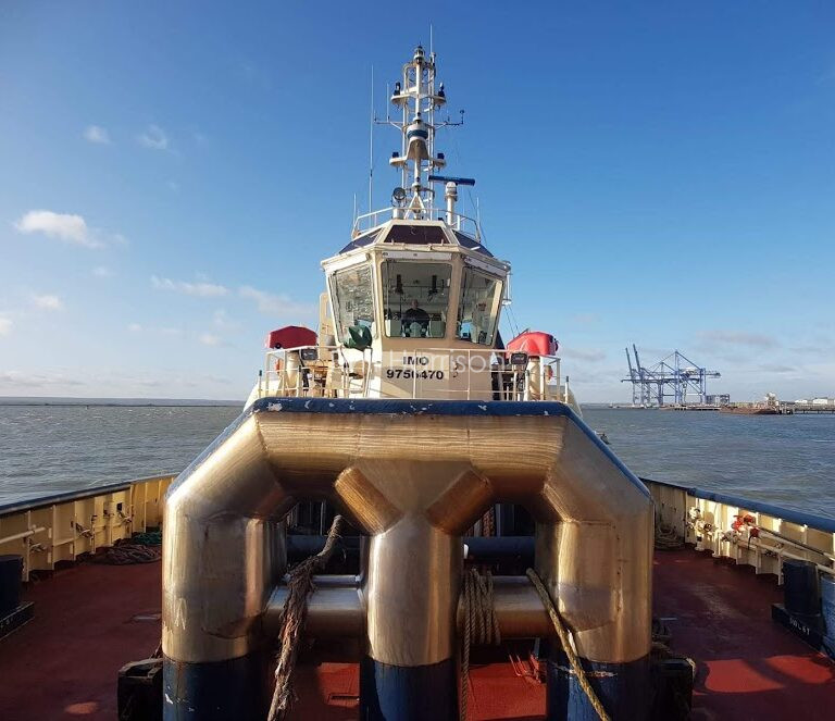 Onboard a ship, looking up at Phil at the helm. Water and blue sky in the background.